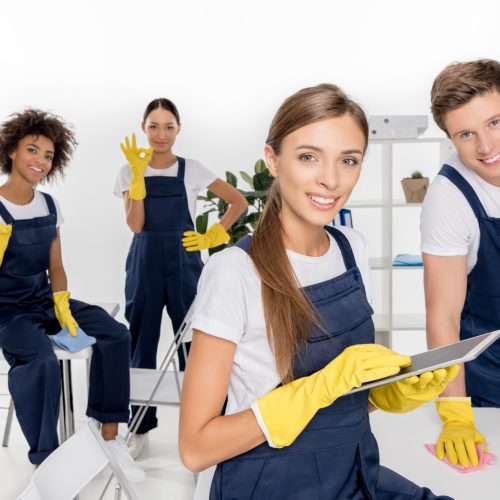 smiling young female cleaner using digital tablet while colleagues working behind